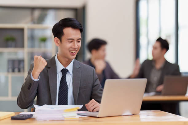 asian businessperson using laptop and celebrating victory and success, have good news, job celebrating achievement. - news of the world imagens e fotografias de stock