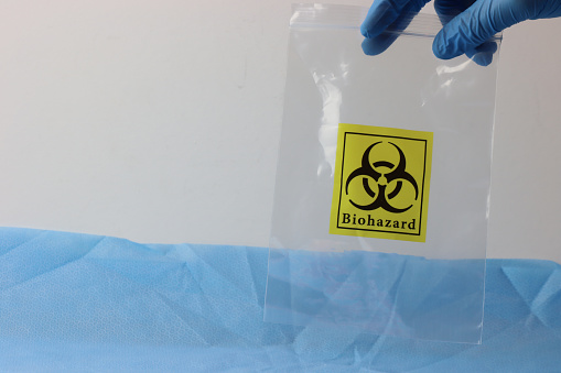 Empty biohazard bag holder by a healthcare professional wearing gloves. Copy space on the bag side