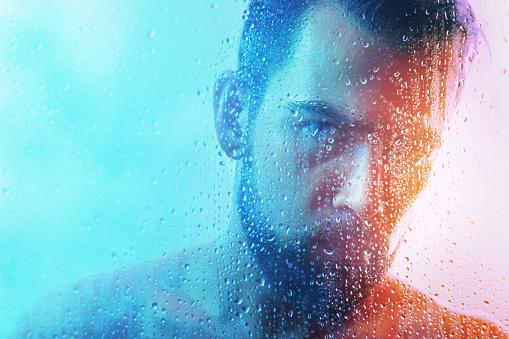 Portrait of handsome young man captured through wet glass in blue and orange light.