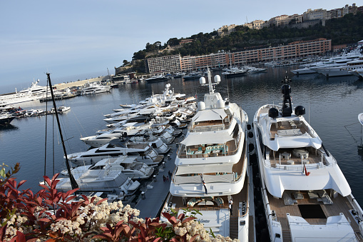 Luxury yachts berthed in the Port Hercules harbour of  Monaco Monte Carlo. In the background overlooking the harbour is the Rock of Monaco where Monaco-Ville, the oldest part of Monaco, and the Prince's Palace can be seen against the skyline of a clear blue sky