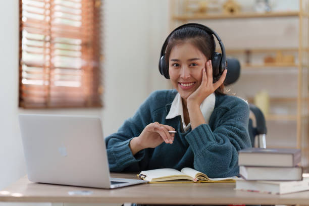 istock Online education, e-learning. Asian woman in stylish casual clothes, studying using a laptop, listening to online lecture, taking notes, online study at home 1486894749