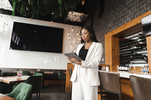 Concentrated biracial young woman with digital tablet and working at a bar restaurant