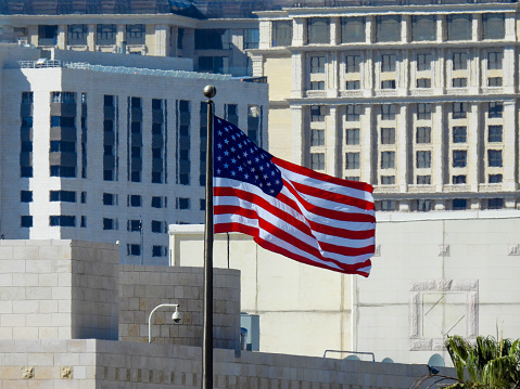 The Stars and Stripes flying at the Embassy of the United States of America in Abdoun, Amman.   In the background are five-star hotels.  This image was taken from the US Embassy Circle in the afternoon on a sunny day on 1 May 2023.