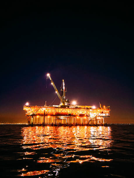 des lumières vibrantes et de haute intensité brillent sur une plate-forme de forage pétrolier illuminée la nuit dans l’océan pacifique, reflet de jolies lumières dans l’eau - oil rig sea drill petroleum photos et images de collection