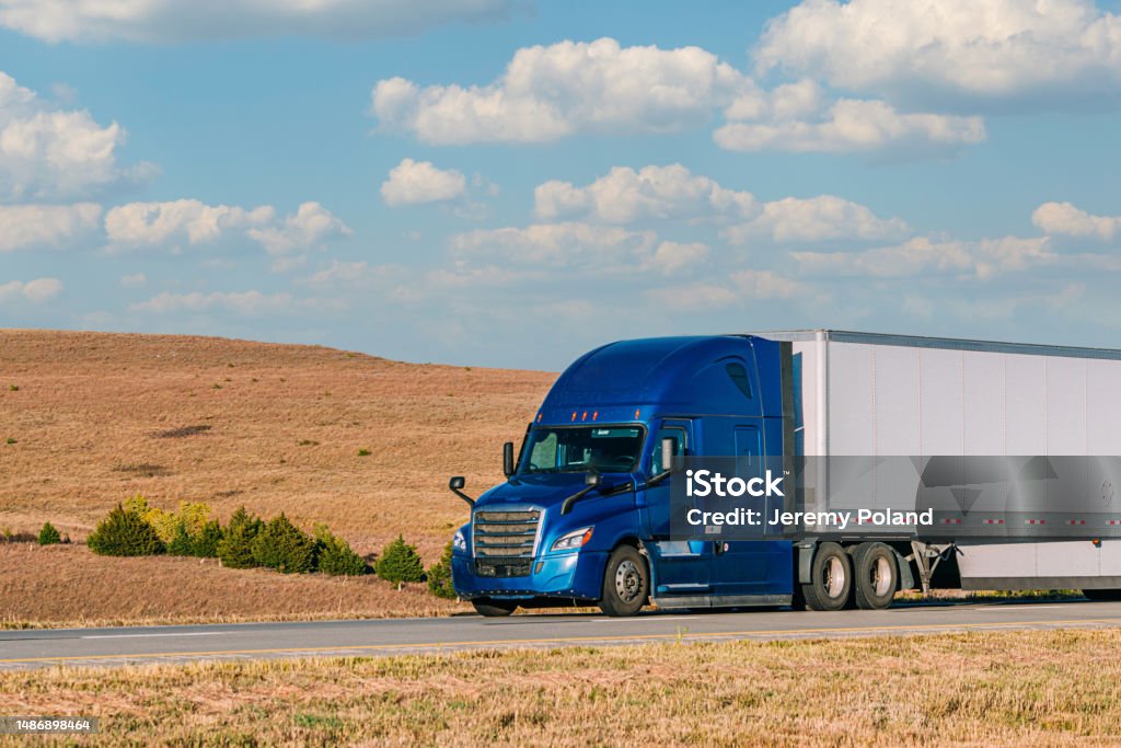 Close-Up Shot of a Royal Blue Semi Truck Driving on I-70 West across Kansas on a Sunny Day Driver's Point of View of an American Conventional Cab-Forward Semi Truck Driving on Interstate 70 across the Plains of Kansas on a Sunny Day Asphalt Stock Photo