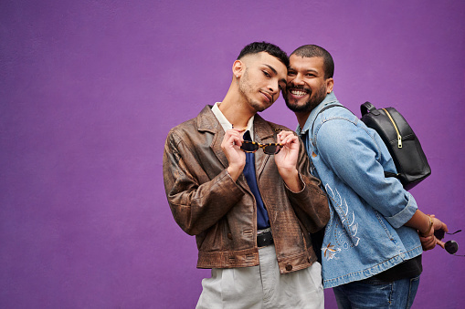 Portrait of a stylish young gay couple smiling and posing together in front of a purple wall outdoors