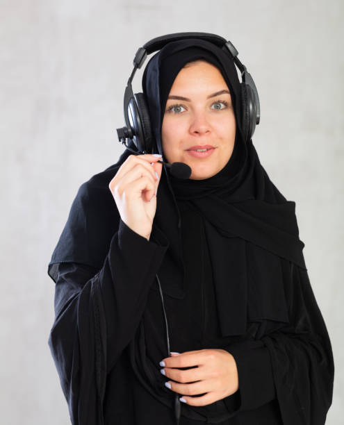 smiling Muslim woman in black hijab and headphones with microphone on gray background. smiling Muslim woman in black hijab and headphones with microphone on gray background.Female call center employee in traditional Muslim clothing azerbaijani culture stock pictures, royalty-free photos & images