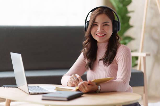 istock Online education, e-learning. Asian woman in stylish casual clothes, studying using a laptop, listening to online lecture, taking notes, online study at home 1486900499