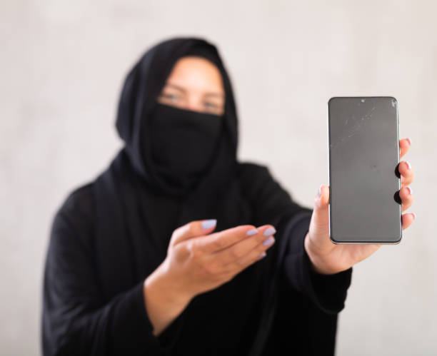 young Muslim girl with her face covered by burka shows empty dark smartphone screen. young Muslim girl with her face covered by burka hold in hand use close up mobile cell phone with blank screen workspace area azerbaijani culture stock pictures, royalty-free photos & images