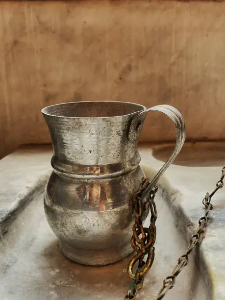 Traditional pewter tankard chained to marble counter in orthodox church. Baptism ceremony, holy water.