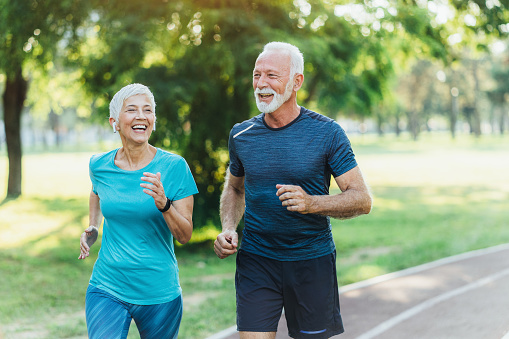 Couple of Mature people jogging together. Senior woman and men, friends or couple having great time together jogging outdoor in the nature. Running in park and using smart technologies