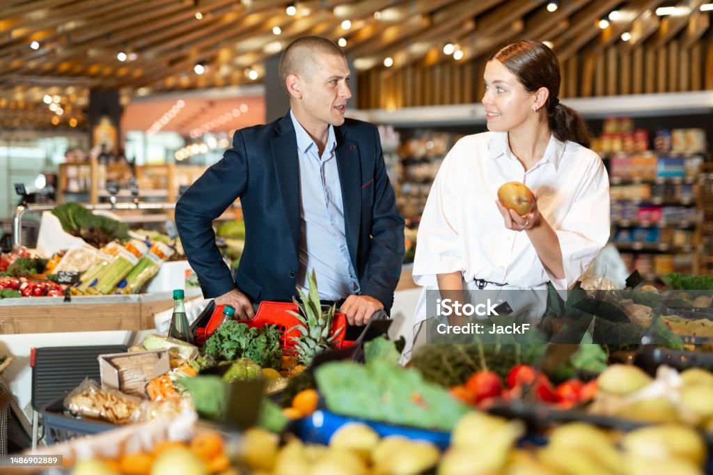 Positive young couple with a grocery cart in the supermarket, choose pears Positive young couple standing near the counter with a grocery cart in the supermarket, choose pears 18-19 Years Stock Photo