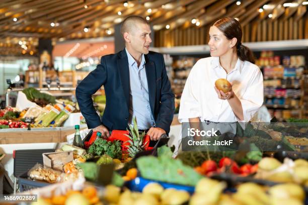 Positive Young Couple With A Grocery Cart In The Supermarket Choose Pears Stock Photo - Download Image Now