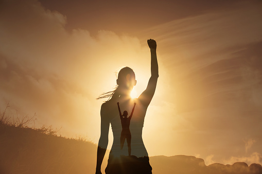 Strong motivated female on a mountain top with fist up celebrating victory