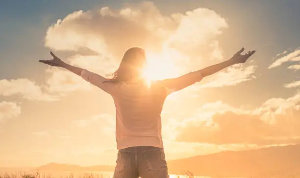 Photo of Young woman with hands up the morning sun light finding happiness, peace and hope in nature