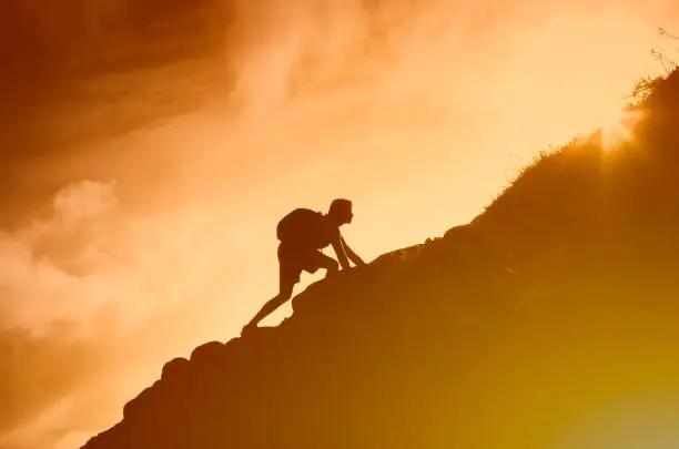 Photo of Man climbing up mountain cliff. Working hard to reach goals