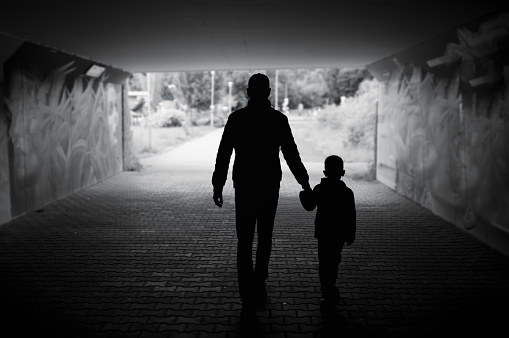 Father and son holding hands waking down dark city street