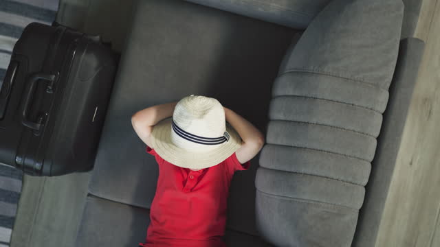 Sweet toddler in hat puts hands behind head lying on sofa