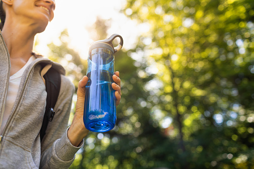Active young woman holding bottle of water hiking in the forest