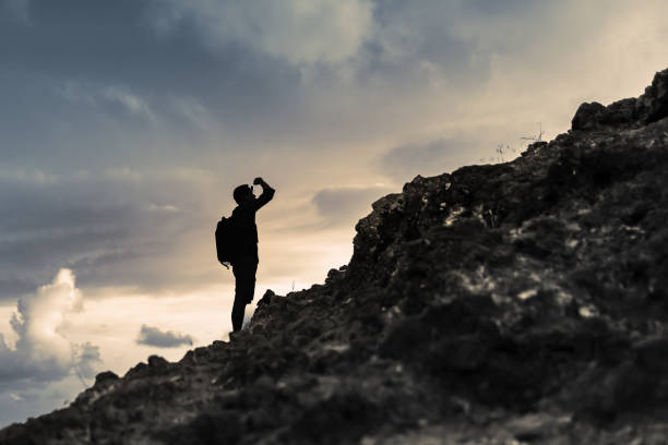 L'uomo si prepara a salire sulla montagna guardando la sfida davanti a lui. - foto stock