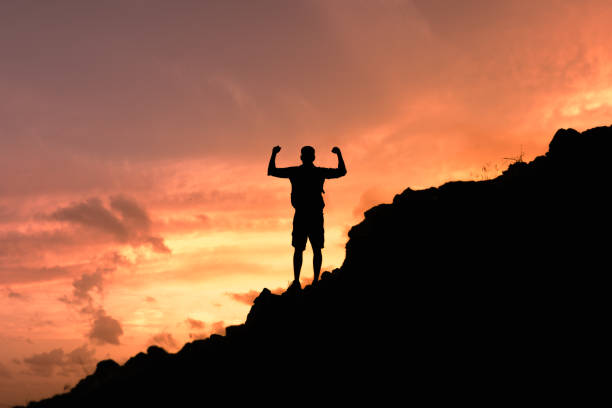 Man standing on the edge of a mountain flexing arms celebrating victory