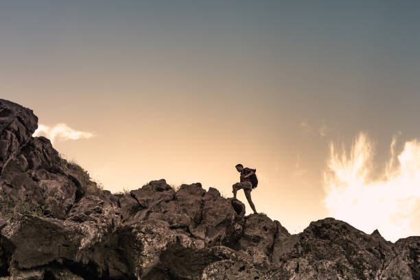 Männlicher Wanderer, der einen felsigen Berg hinaufklettert. Selbstverbesserung und Zielsetzungskonzept. – Foto