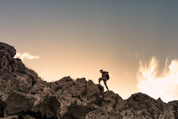 Escursione di sesso maschile che si arrampica su una montagna rocciosa. Concetto di auto-miglioramento e definizione degli obiettivi. - foto stock