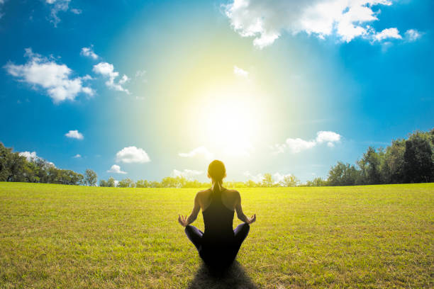 The silhouette of a woman meditating in a grass field with a bright sunny ligh shining upon her.