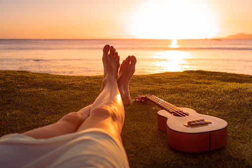 Female sitting on grass next to guitar looking at the sunset view