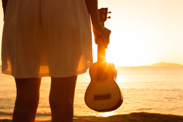 Donna che tiene la chitarra dell'ukulele sulla spiaggia del tramonto - foto stock