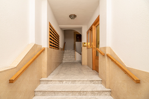 Portal of an urban residential house with veined white marble floors, light oak handrails, mailboxes and matching woodwork