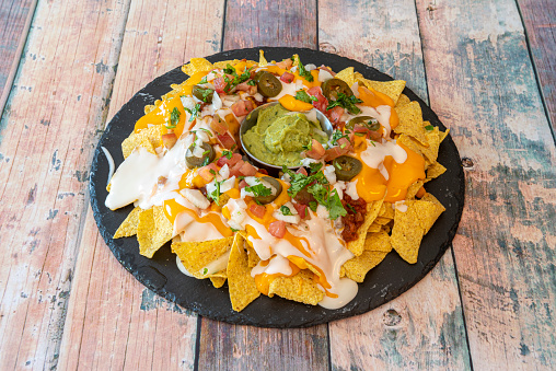 Large portion of Mexican nachos with lots of cheese of two varieties on wooden table