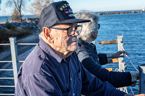 An aging but still active 93 year old World War II and Korean Conflict USA military war veteran and his senior adult woman daughter are sightseeing - standing together side by side looking out over Lake Ontario near Rochester, New York State, USA.
