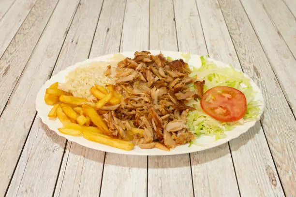 Photo of Kebab menu tray complete with french fries, basmati rice, minced roast chicken meat, onion and iceberg lettuce with tomato on white table.