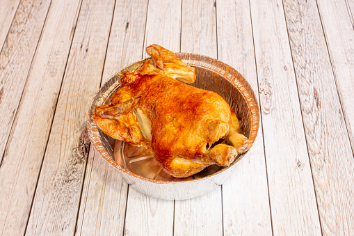Roasted whole chicken in aluminum container for home delivery on white table