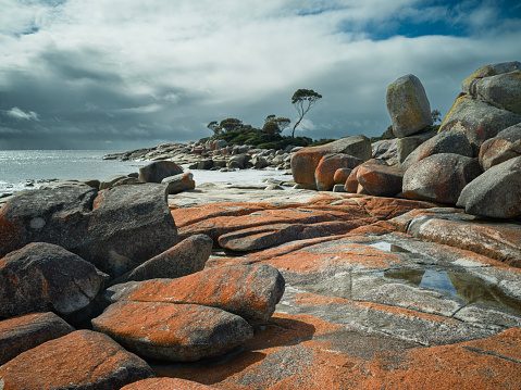 Dramatic sky over the Bay of Fires in Tasmania, red rocks and green blue sea