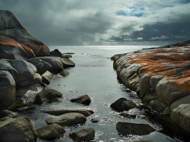 Dramatic sky over the Bay of Fires in Tasmania, red rocks and green blue sea