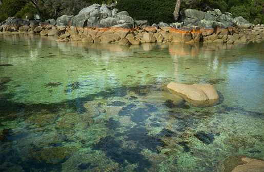 Dramatic sky over the Bay of Fires in Tasmania, red rocks and green blue sea