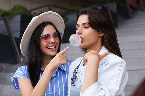 Stylish women having fun and blowing gum near stairs outdoors