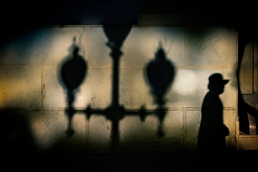 a person walking on a sidewalk and heavy shadows against a house wall an after dinner in alicante city in spain -