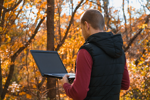 A freelance man works remotely in nature in the autumn forest. Country life. A break from civilization. Van Lifevibes. A man with laptop. Distance learning in the fresh air via a laptop. Remote work.