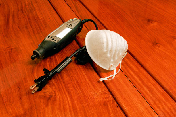 An electric rotary tool and dust mask placed on a rosewoord table. The cable is rolled up and strapped. Photograph. No people. Note to Inspector: all logos and model numbers have been removed.