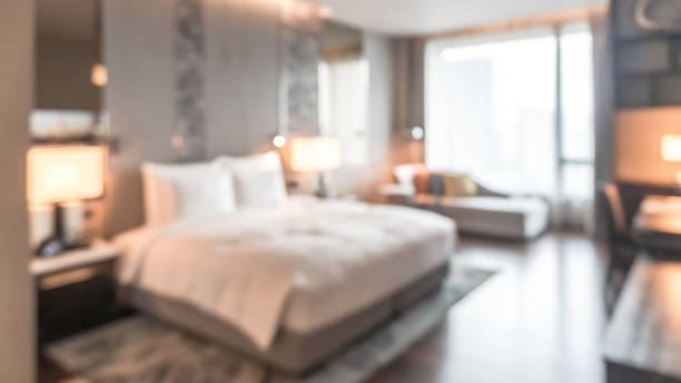 istock Hotel bedroom blur background guest room interior with blurry comfortable king size bed white, bedsheet, TV, work table desk and chair furniture 1486949025