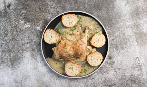 istock Stewed chicken leg with garlic and bread  on a round plate on a dark grey background. Top view, flat lay 1486973553