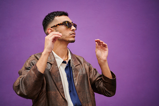 Young man wearing a stylish pair of sunglasses while standing in front of a purple background outdoors