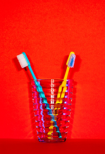 close up of two embracing toothbrushes in a glass on red background