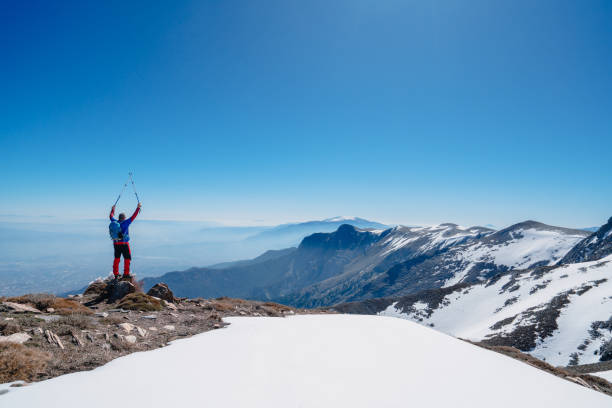 Alpinist climber is proud of himself while standing on snowy mountain crest on extreme harsh conditions.