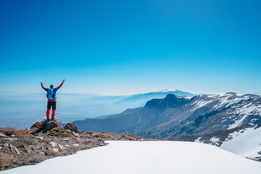 Alpinist climber is proud of himself while standing on snowy mountain crest on extreme harsh conditions.