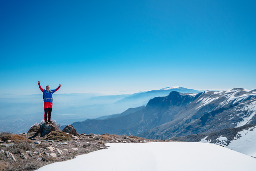 Alpinist climber is proud of himself while standing on snowy mountain crest on extreme harsh conditions.