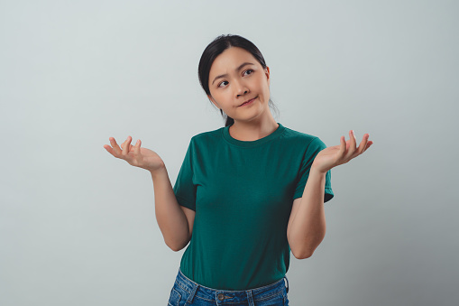 Asian woman angry annoyed and shrugging shoulders standing isolated over background.